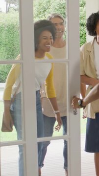 Vertical video: Opening door, khaki host greeting arriving friends with cardboard carrier in entry
