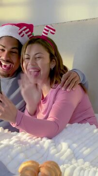 Vertical video: Receiving call, couple holding phone in bed, in Santa hat, waving to greet family