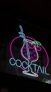 Neon cocktail sign with glowing tropical drink glass, bright pink circle, blue straw, green cherry accents, and dark nightlife background for bar and restaurant decor