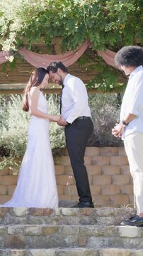 Vertical video: Swapping ring, bride in dress and groom hugging on stone steps, friend celebrating