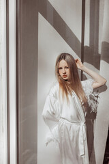 Fototapeta premium A girl in a white coat against a white wall. A ray of light from the sun