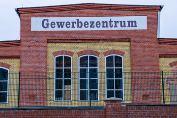 Obraz premium Front view of a restored historic brick industrial building now used as a commercial center (Gewerbezentrum) in Germany. The symmetrical facade combines red and yellow brickwork with arched windows.