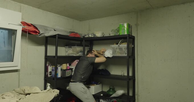 Man reaching for items on a storage shelf while objects fall toward his head. Concept of household accident, falling objects, risk, workplace safety, and storage hazards.
