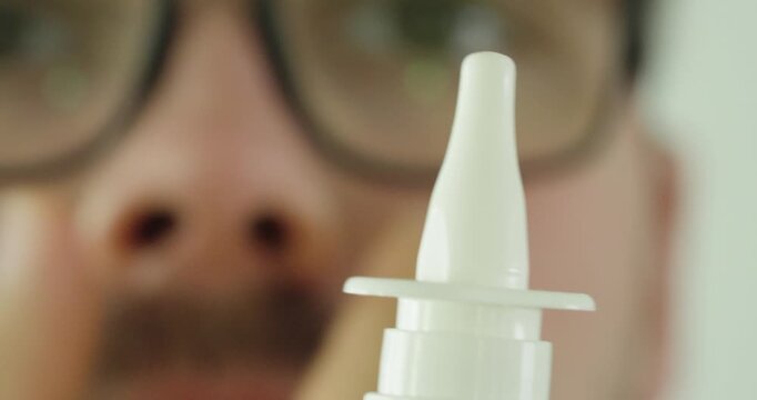 Extreme macro view of a nasal spray applicator with a blurred man and nose in the background. Concept of nasal care, allergy treatment, respiratory health, medication, and healthcare.