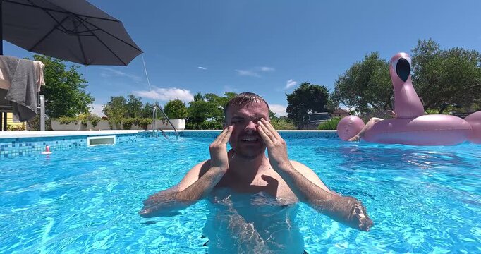 A man in a swimming pool reacting to burning eyes caused by chlorine in the water. Focus on water quality, chemical sensitivity, and swimming comfort in a resort environment.