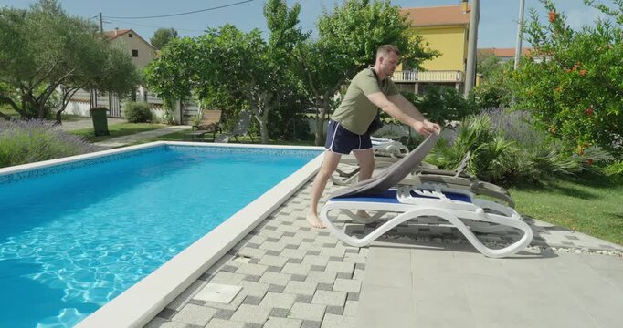 A man placing a towel on a sun lounger by the pool to reserve it, illustrating a common rule violation in resort areas. Focus on pool etiquette, fairness, and guest behavior.