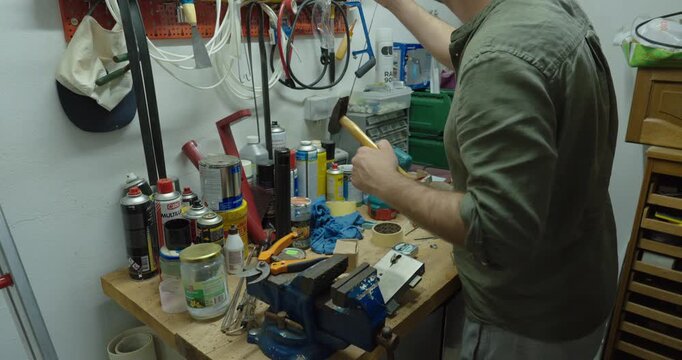 Man working at a cluttered workshop bench with tools and equipment, performing a repair or DIY project. Ideal for concepts of craftsmanship, maintenance, engineering, manual labor, home improvement, a