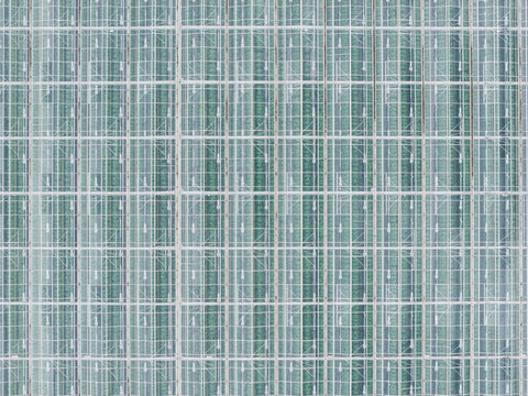 Aerial view of a large industrial greenhouse with a repeating grid pattern of glass panels and visible green crops inside in Rumbula, Ropazi Municipality, Latvia.