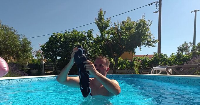Man in a pool holding up swim trunks as a pool rules concept.