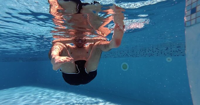 Man underwater performing ear pressure equalization while diving in a swimming pool.