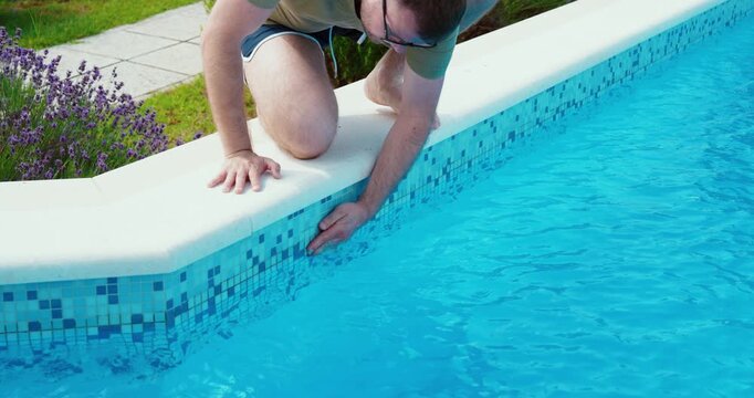 Person inspecting the pool wall by hand to check cleanliness and maintenance.