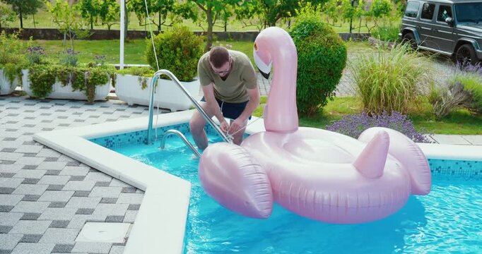 Man securing an inflatable flamingo float to prevent it from drifting away.