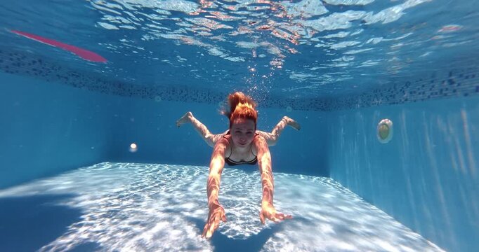 Woman swimming underwater in a pool during a summer leisure activity.