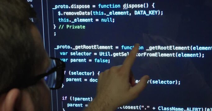 Close-up of a software developer reviewing source code and pointing at the screen while searching for programming errors. Technology, debugging, and software development concept.
