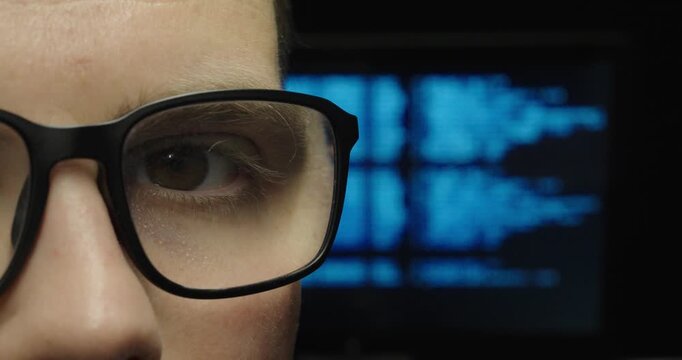 Close-up of a person wearing glasses carefully following code with their eyes while analyzing information on a computer screen. Technology, programming, concentration, and software development concept