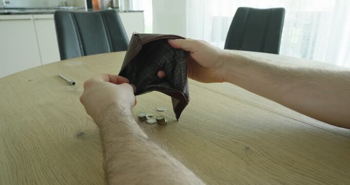 Person holding an empty wallet at a table, symbolizing financial hardship, rising living costs, inflation pressure, debt concerns, and personal budget challenges.