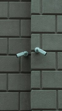 Two white security cameras mounted on textured concrete wall, angled in different directions, creating modern surveillance concept with geometric background and urban security setting