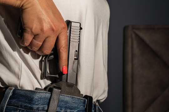 Close up of a woman drawing a semi automatic handgun pistol from an inside the waistband IWB holster for concealed carry protection