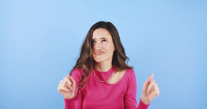Young woman pointing finger at camera asking a question then gesturing thumbs down to show disapproval and rejection isolated on blue background, concept of doubt, disagreement and negative feedback