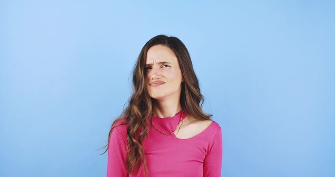 Young woman making skeptical and annoyed facial expressions, showing reluctance and doubt with mimical gestures portrait isolated on blue background, concept of uncertainty, refusal, and critical mood