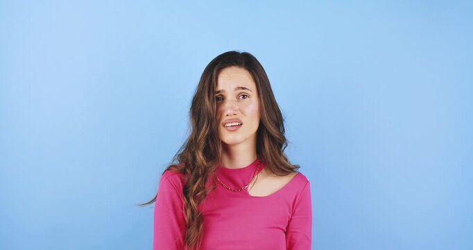 Young woman showing an angry, aggressive, and frustrated facial expression, reacting negatively, portrait isolated on blue background, concept of extreme irritation, conflict, and strong disapproval