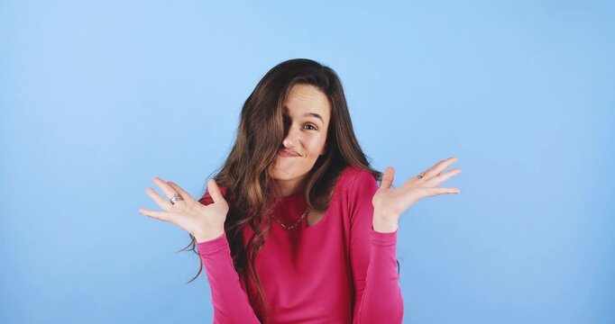 Young woman looking surprised and confused, making an oops facial expression with wide eyes and open mouth, hand near face, isolated on blue background, concept of mistake and sudden realization
