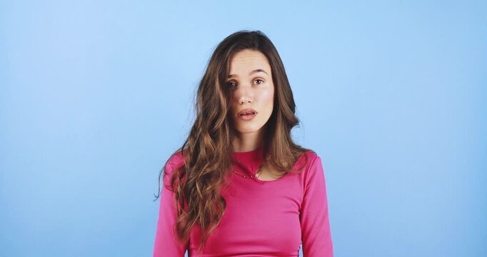 Young woman making a stern no gesture with index finger, showing disagreement and refusal with serious facial expression, warning sign isolated on blue background, concept of restriction and rejection