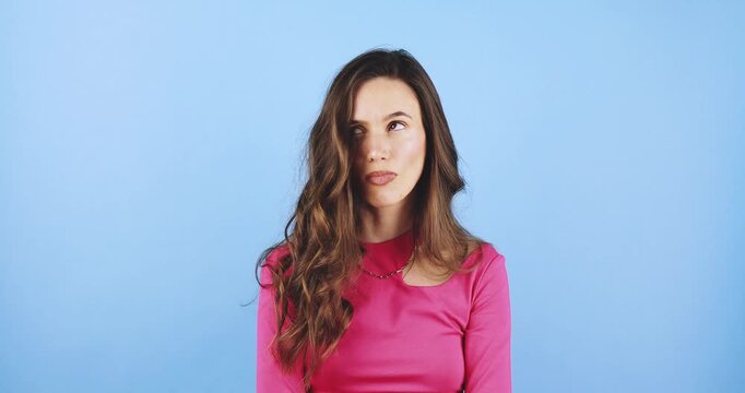  Young woman looking annoyed with rolling eyes and bored facial expression, showing indifference and skepticism, studio on blue background, concept of apathy, bad mood, and lack of interest