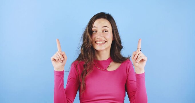 Young woman looking up with curiosity, suddenly realizing something with a joyful expression, pointing fingers upwards studio portrait isolated on blue background, concept of inspiration and good idea