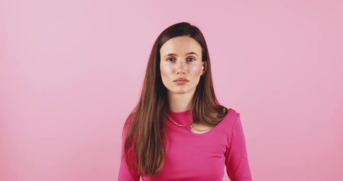 Young woman looking around with skeptical and suspicious facial expression, pointing fingers up with doubt and confusion, studio isolated on pink background, concept for mistrust and uncertainty