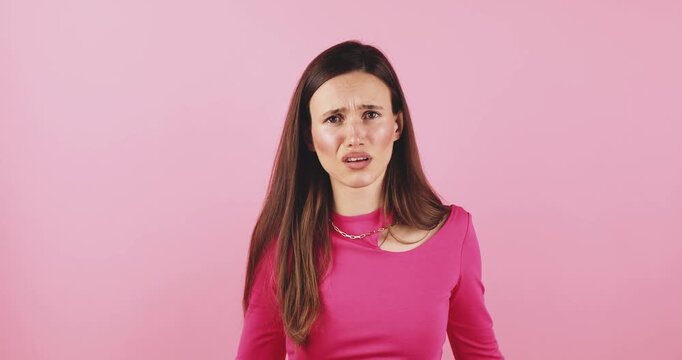 Young woman with long brunette hair expressing confusion and frustration, looking at camera with questioning facial mimicry, studio portrait isolated on pink background, concept for misunderstanding