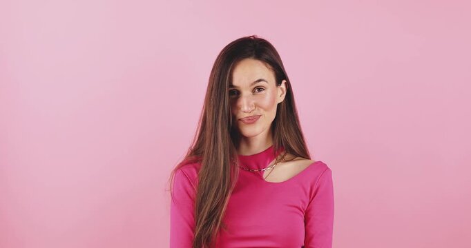 Young woman looking around with playful, mischievous, and thoughtful expression, biting her lip and glancing sideways, studio portrait isolated on pink background, concept for curiosity and flirtation