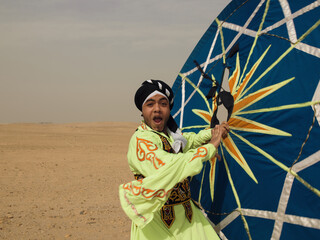 Fototapeta premium Energetic Egyptian tanoura folk dancer in vivid green costume spinning a large patterned skirt prop in the open desert ideal for cultural festival and