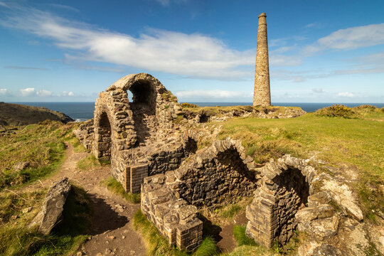 Ruined stone structures calciner labyrinth and chimney stack of Botallack Mine under a blue sky in Cornwall