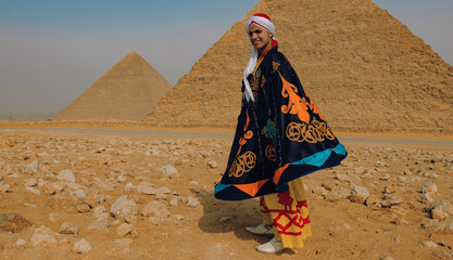 Fototapeta premium Joyful young Egyptian tanoura folk dancer twirling a colorful ornate cape in front of the Giza pyramids ideal for Egypt tourism cultural festival and