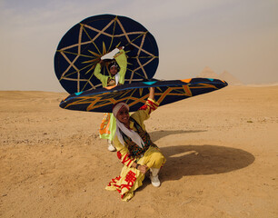 Fototapeta premium Energetic Egyptian tanoura dancers in vibrant costumes spin colorful skirts overhead in the desert before the Giza pyramids ideal for cultural tourism