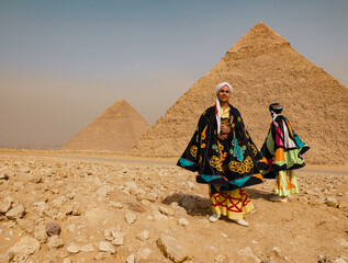Fototapeta premium Festive Egyptian folk dancer in a colorful embroidered tanoura costume and turban standing proudly before the Giza pyramids in the sunny desert ideal