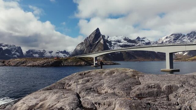 Concrete bridge spanning fjord with rocky shoreline and snow capped mountains