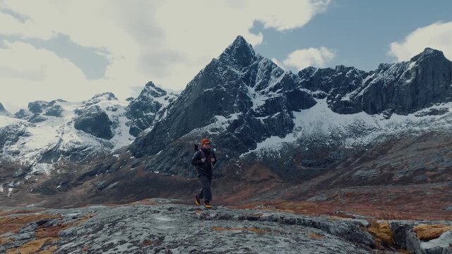 Lone hiker on rocky alpine plateau facing snow-capped peaks under moody sky