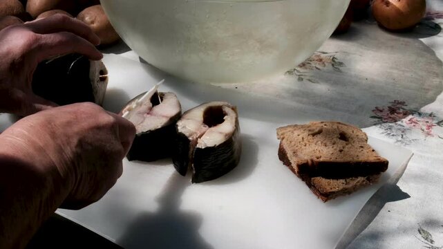 cutting off a piece of smoked mackerel in the Sunny World on a rustic table outside eating mackerel with bread outside after gardening. High quality 4k footage