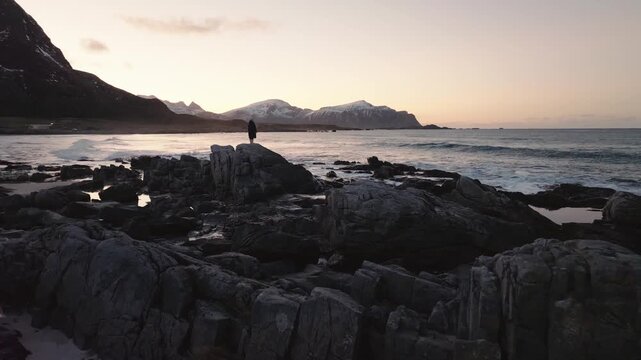 Solitary person on rocky coast at sunset with mountain backdrop