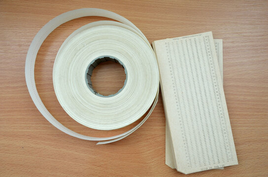 Vintage computer data storage: punched tape reel and stack of punch cards on wooden background
