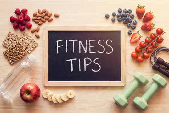 Flat lay of healthy food dumbbells and a chalkboard reading fitness tips