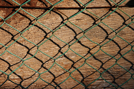 Close up of chain link fence against natural wooden background. Geometric pattern texture suitable for industrial, security and urban concepts.