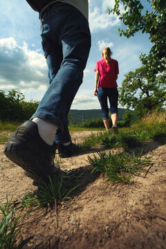 Two people, a woman and a man, hiking on a sunny path in the countryside. Closeup of a hiker's foot while walking.
