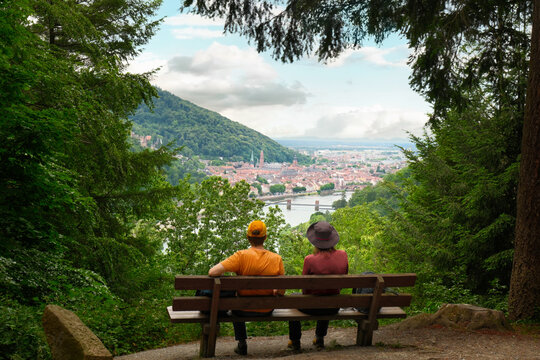 Tow people in a forest sitting and relaxing on a bench with a spectacular view on the scenic town of Heidelberg, Germany.