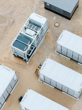 Aerial view of industrial battery storage containers and power units arranged in a gravel yard in Suntazi, Ogre Municipality, Latvia.