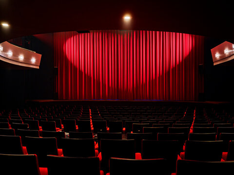 Red stage curtain and empty seating rows in a theater auditorium with warm stage lighting, a performing arts hall interior