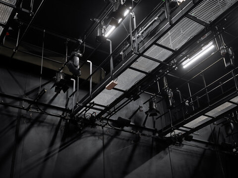 Network of lighting trusses and spotlights above a stage in a darkened venue, complex technical rigging for live productions