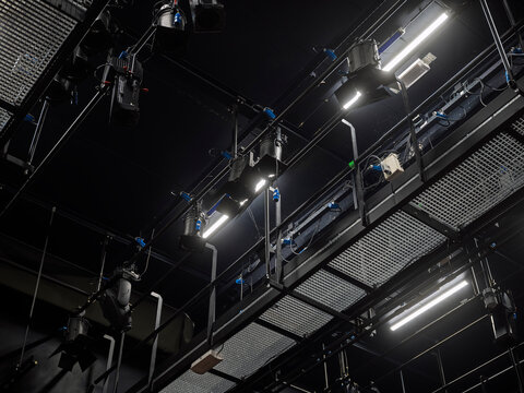 Dark theater ceiling filled with lighting trusses, rigging and spotlights, the technical backbone of a stage production venue